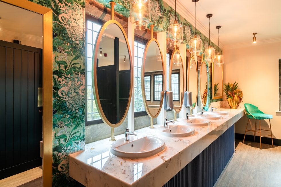 Modern washroom with large oval mirrors and green decorative wallpaper