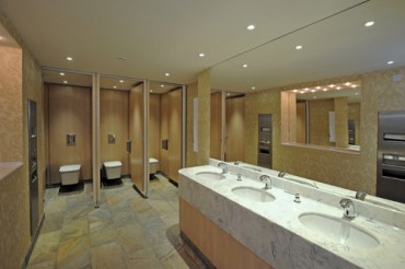 Public bathroom with marble look vanity top with multiple undermounted wash basins.