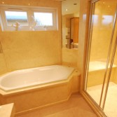 White diamond shaped bath with large walk in shower with cream marble finish.