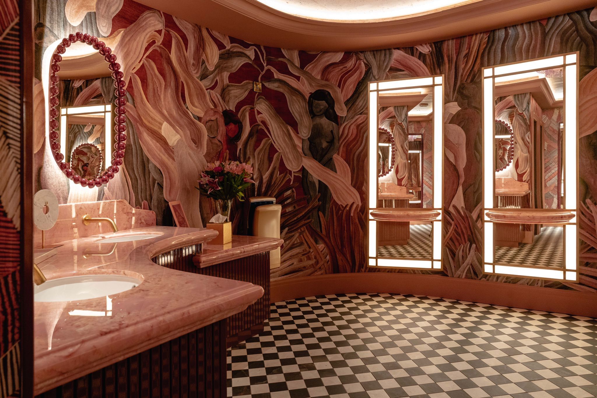 a pink bathroom with led backlit mirrors, bold botanical pink and green wallpaper with pink marble vanities