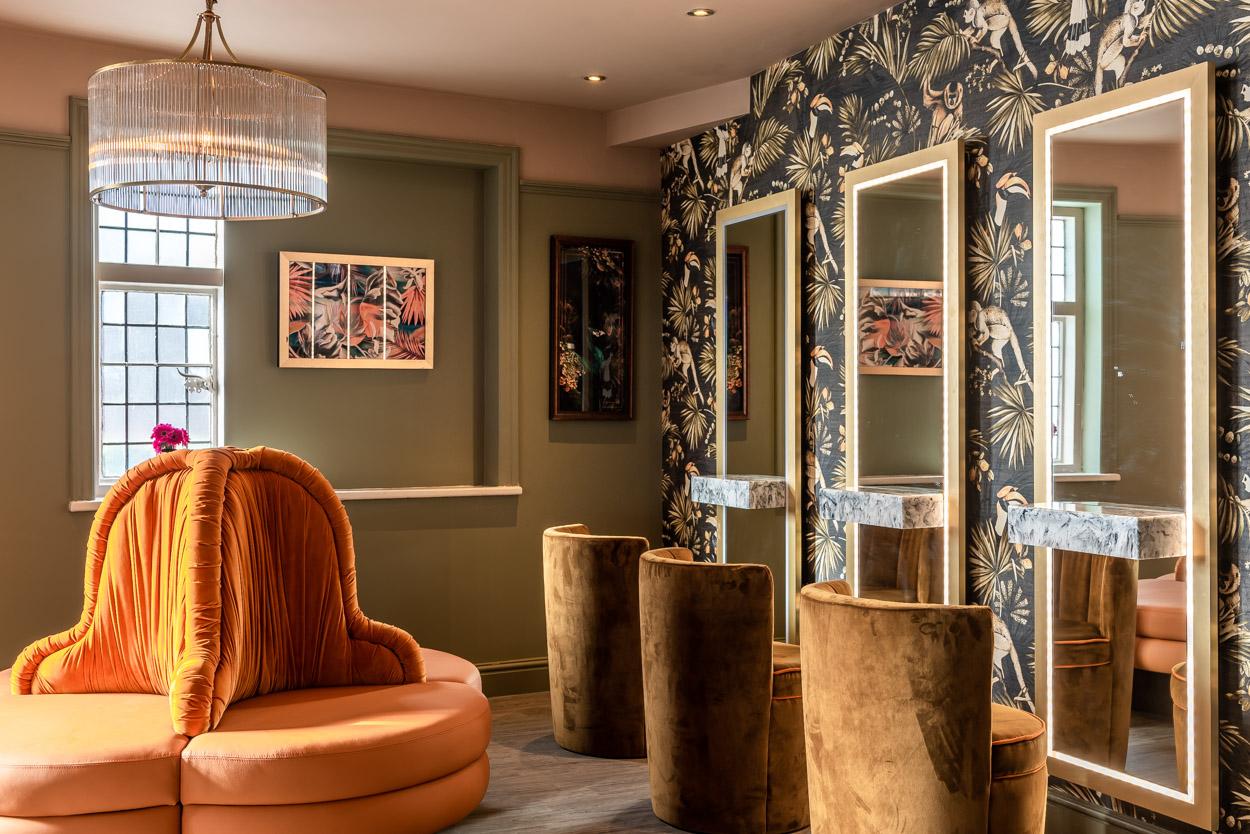 Luxury makeup area to ladies washroom with large mirrors and orange sofa seating