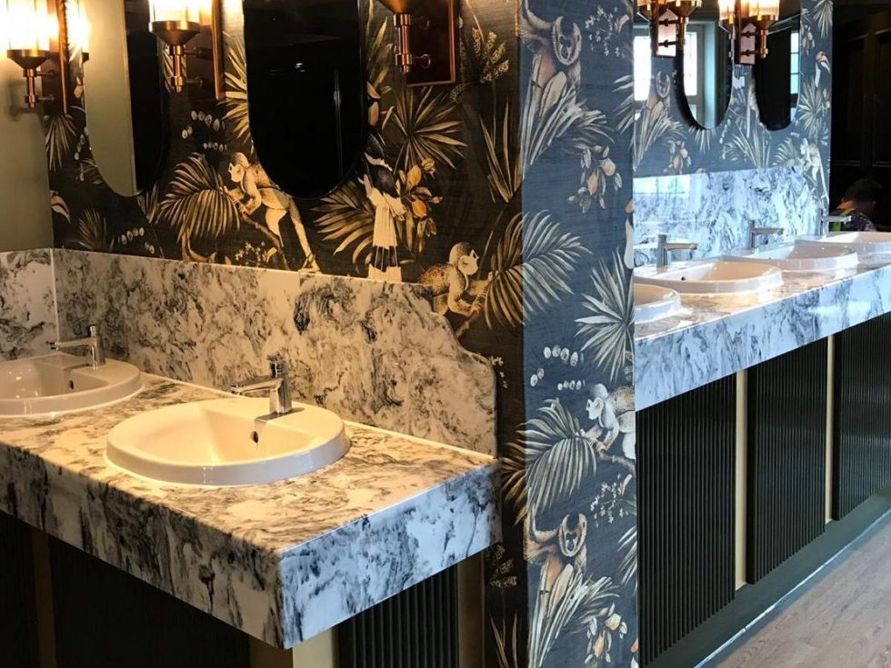 White and black veined wash room vanities with jungle themed wallpaper