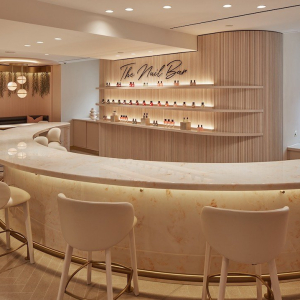 a neutrals nail salon with scalloped cream chairs, a cream and orange marble bar top and a wall with the nail varnishes displayed