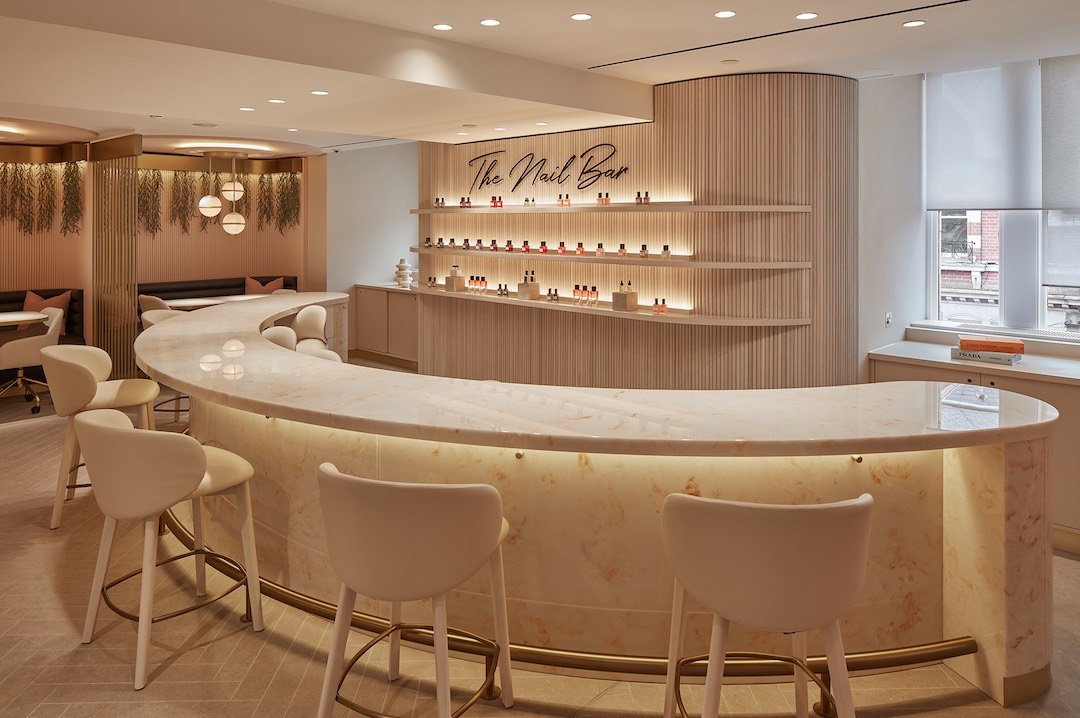 a neutrals nail salon with scalloped cream chairs, a cream and orange marble bar top and a wall with the nail varnishes displayed
