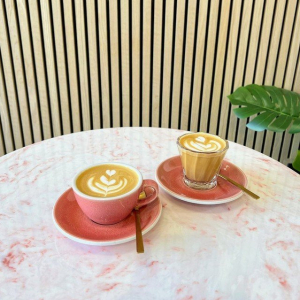 2 pink coffee cups and saucers with a coffee in them,. a white marble table with a pink vein throught out