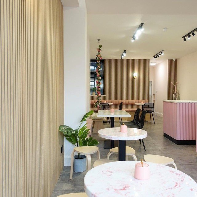 a coffee shop with pink and white marble tables and white stools. with a wooden texture along the walls