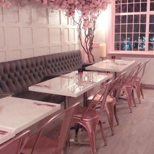 a dimly lit cafe with a cherry blossom tree going up the wall and along the ceiling. pink metallic chairs and white tables.