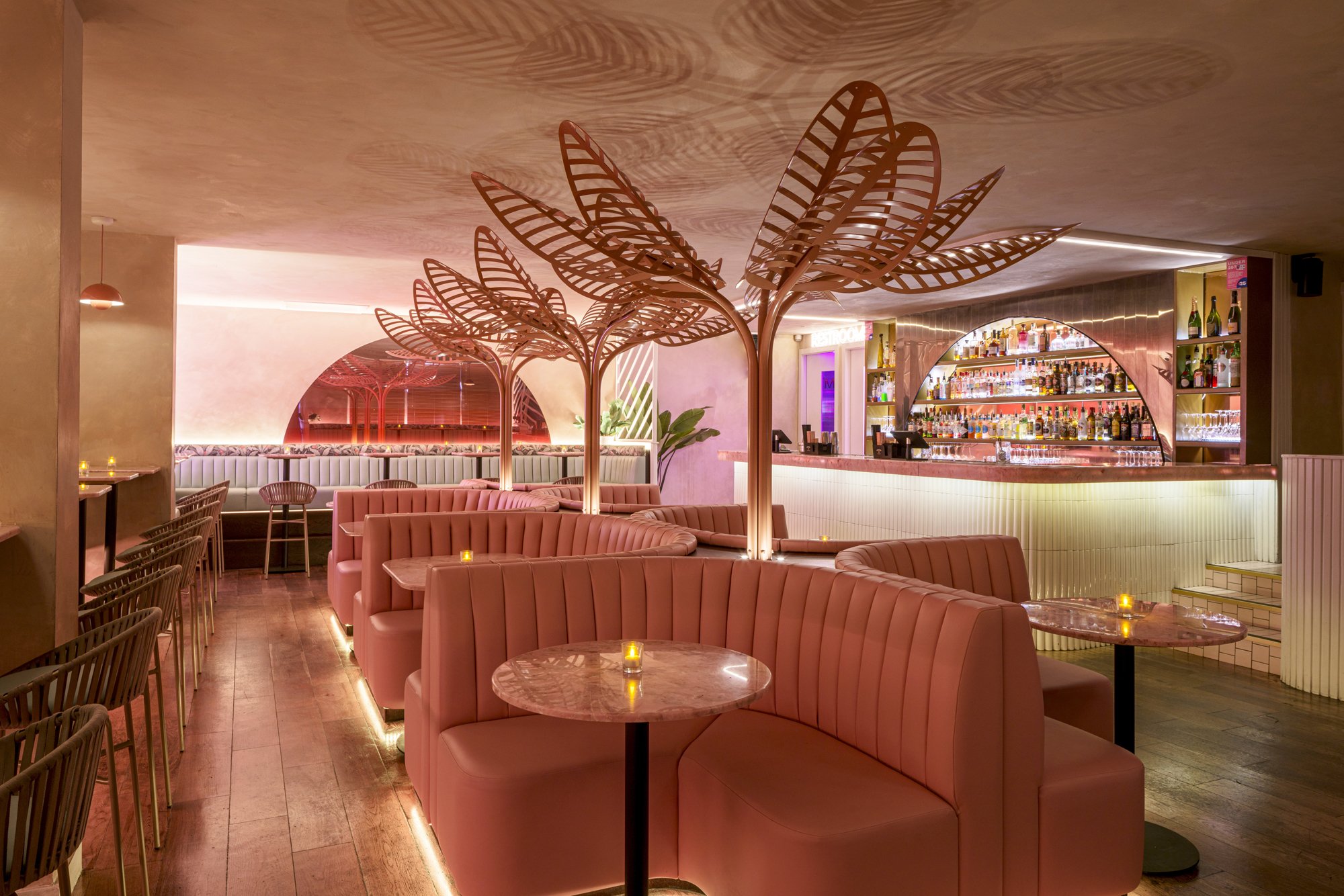 pink bar with pink booth seating, pink wire palm trees and pink marble tables.