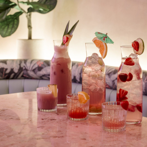 multicoloured cocktails in jugs on top of a pink marble table top