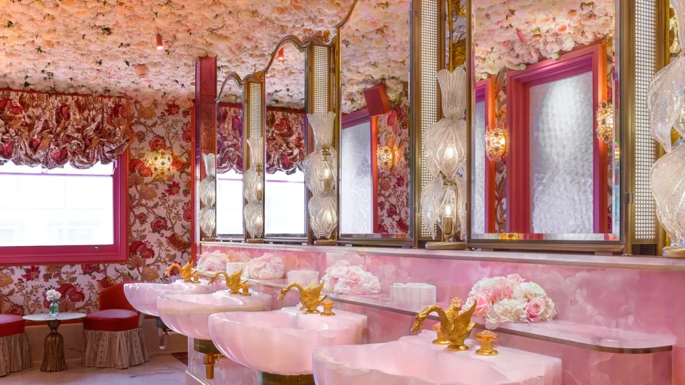 Pink washroom in Annabels with bold floral wallpaper and art deco mirrors and individual clam shell pink sinks with gold swan shaped faucets.