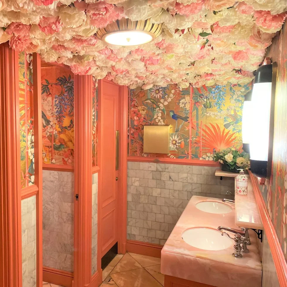 Pink and gold washroom with botanical wallpaper and flowers overhead on the ceiling.