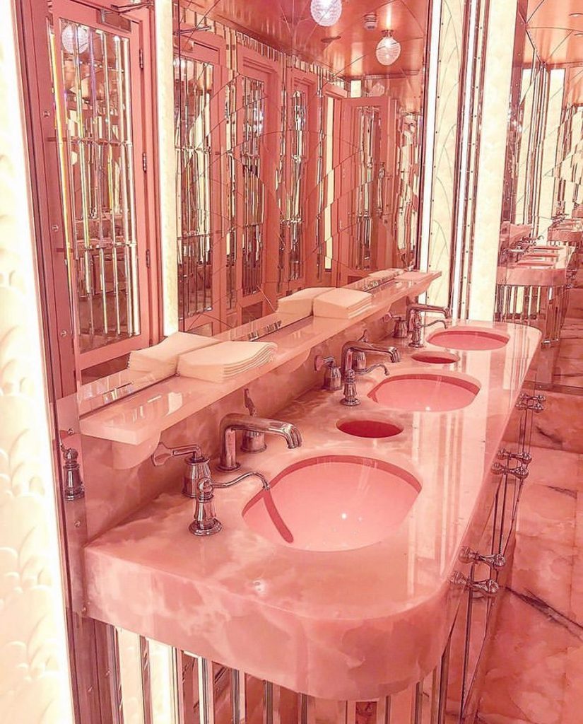 Pink marble washroom with a pink marble vanity top and reflective mirrors around the washroom and along the bottom of the vanity.