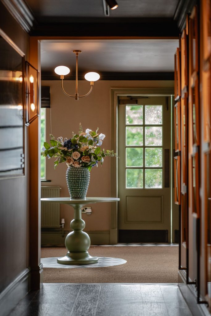 Entry way to a classic bar with touches of natural wood and shades of sage. With a large bouquet of flowers.