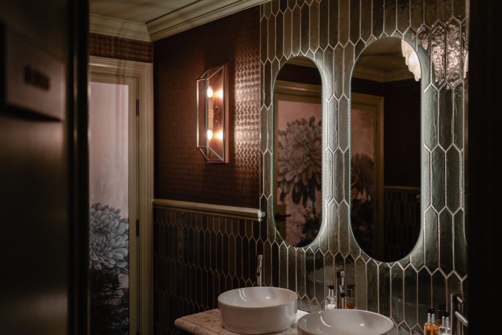 Contemporary washroom with a bespoke marble vanity top and back-lit large oval mirrors and tiling on the wall.