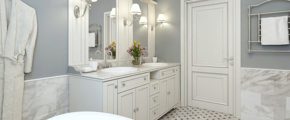 Cream and white classic bathroom with bright lighting around mirrors on the wall and classic white wooden vanity top.